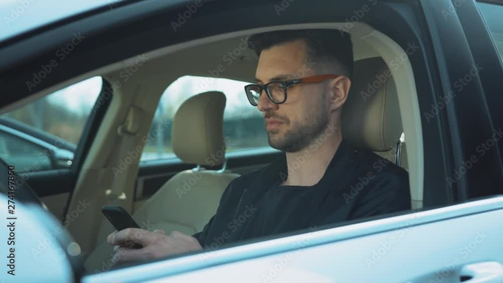 Serious concentrated man in sunglasses sitting at driver's seat in car and chatting. Businessman. Daytime. New car. Automobile. Idea, concept, innovation, message, communication, holding, messaging Serious concentrated man in sunglasses sitting at driver's seat in car and chatting. Businessman. Daytime. New car. Automobile. Idea, concept, innovation, message, communication, holding, messaging