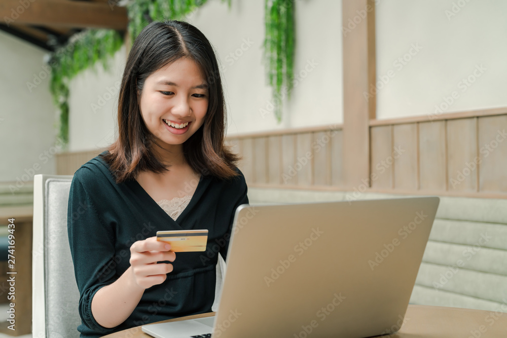 Closeup Asian beautiful woman Wearing a black shirt Sitting in the house Have a credit card in hand Is buying online products with a laptop computer Closeup Asian beautiful woman Wearing a black shirt Sitting in the house Have a credit card in hand Is buying online products with a laptop computer