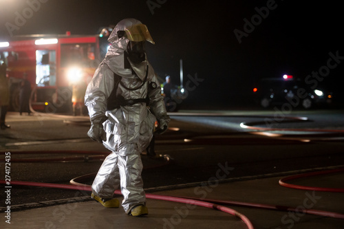 firefighters in silver suit operating on airport site at night. 
