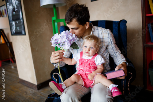 Konstfotografi dad sniffs hydrangea, annual daughter in a pink jumpsuit sits on his lap