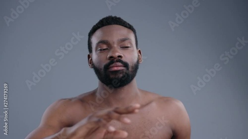 Portrait of topless sexy african american man using a virtual screen swiping pages in air. Young black guy with beard and fit body isolated on grey background. photo