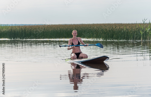 Female Paddler Sitting on a Stand Up Paddle Board on a Still Lake