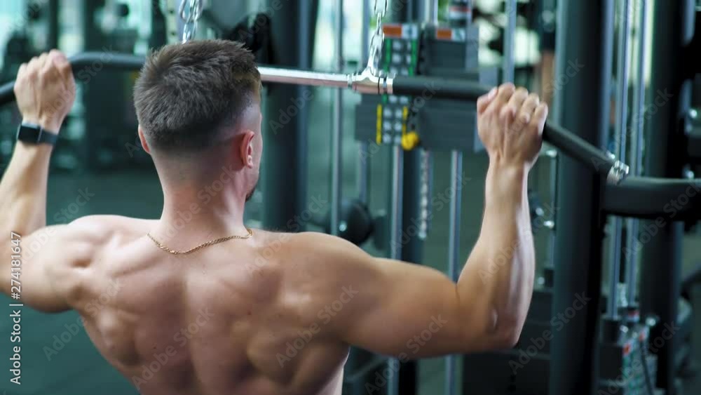 Athlete trains in Gym, lifting blocks on rack machine, back view, training on block device and gym equipment. Athlete trains in Gym, lifting blocks on rack machine, back view, training on block device and gym equipment.