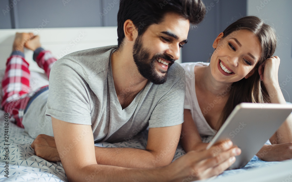 Happy young couple looking a tablet together and laughing while lying on the bed Happy young couple looking a tablet together and laughing while lying on the bed