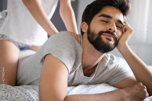 Young woman is doing her handsome boyfriend massage and smiling while they are resting at home
