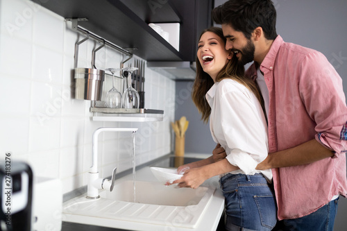 Fotografie Young happy couple is washing dishes while doing cleaning at home