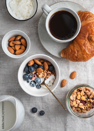 Top view of breakfast table with coffee, croissant, granola, nuts, berries and milk. Flat lay, healthy eating concept.