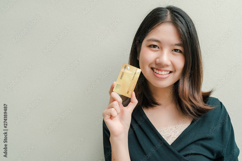 Asian beautiful woman Wearing a black shirt Have a credit card in hand Happy face Standing in the gray wall Asian beautiful woman Wearing a black shirt Have a credit card in hand Happy face Standing in the gray wall