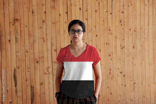 Woman wearing Yemen flag color shirt and standing with two hands in pant pockets on the wooden wall background. photo