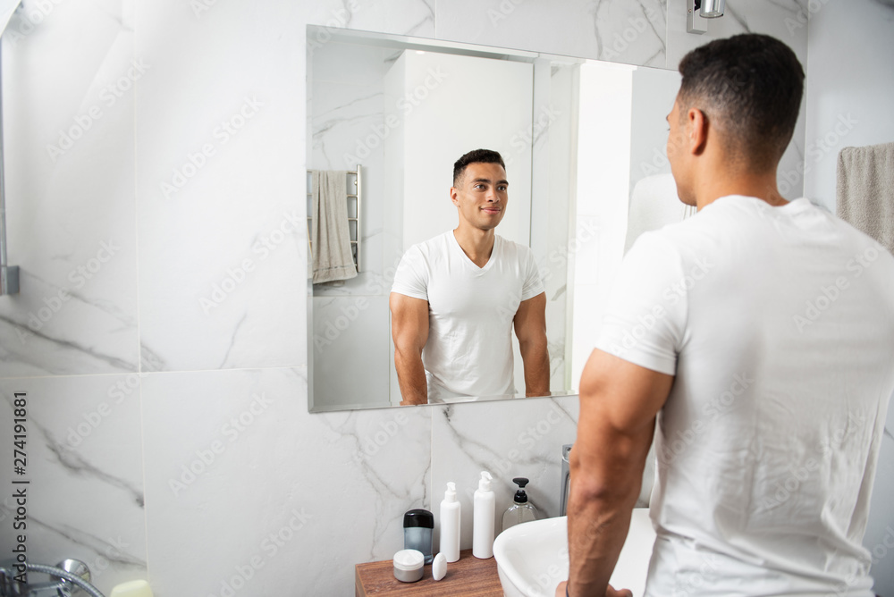 Obraz premium Back side of smiling young man looking at mirror