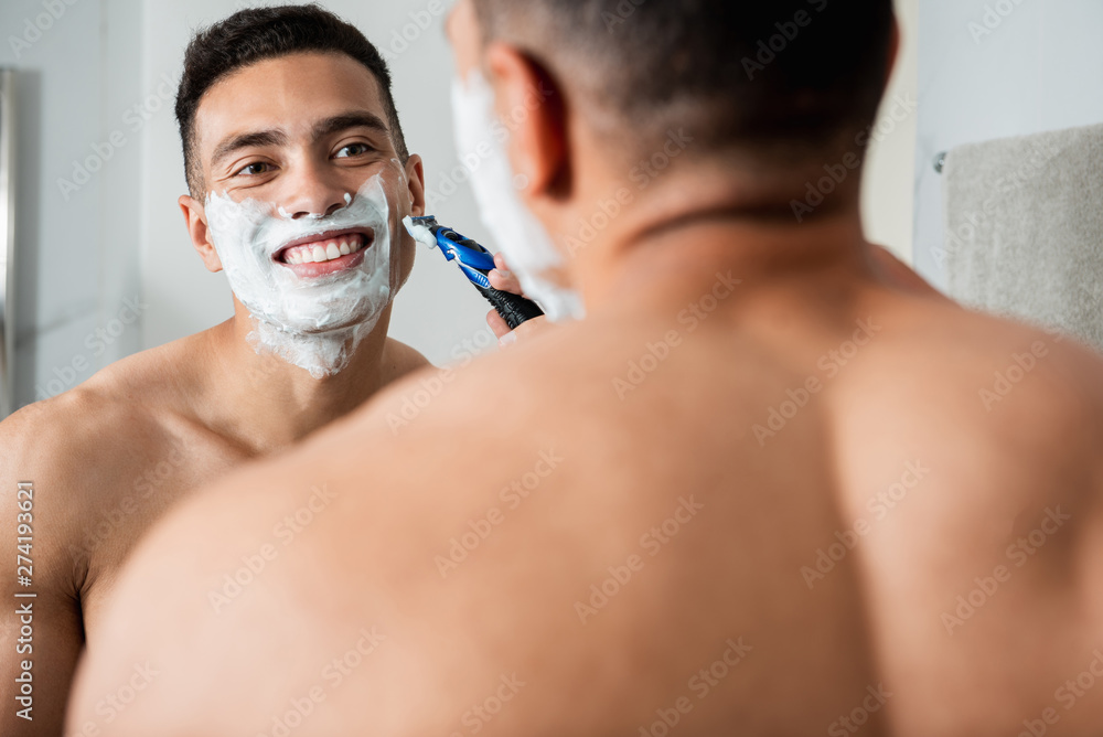 Young happy man shaving himself by razor