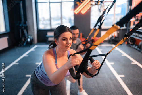 Dark-haired overweight woman feeling tired working out with TRX