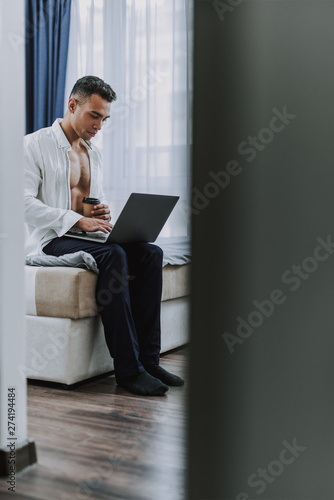 Muscular guy is working on laptop at home