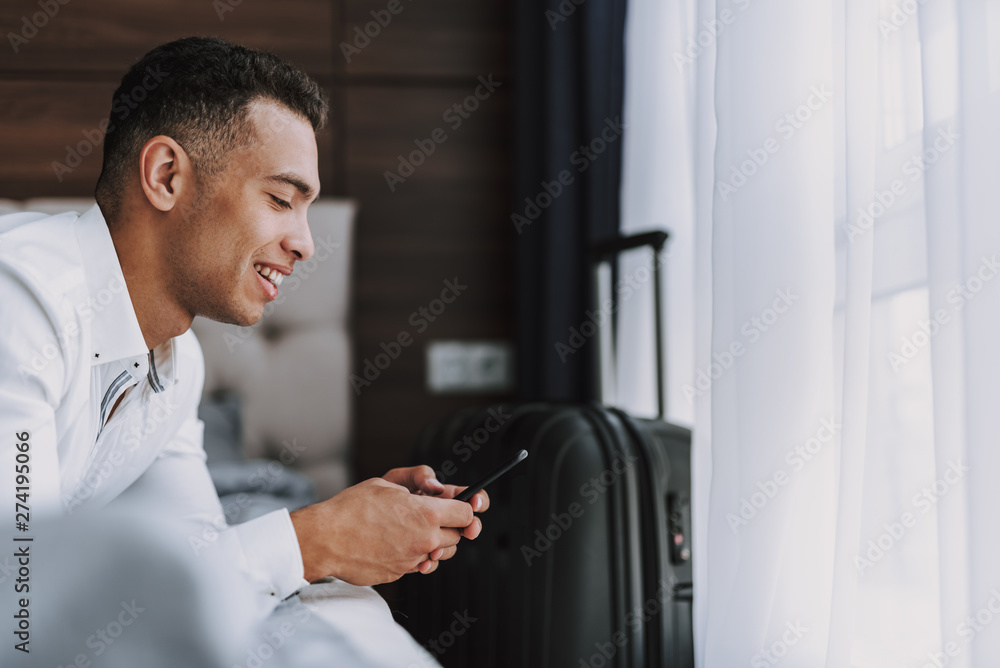 Joyful man is messaging on phone indoors during business trip