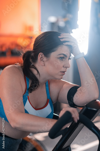 Plump woman feeling exhausted and tired after cycling in gym