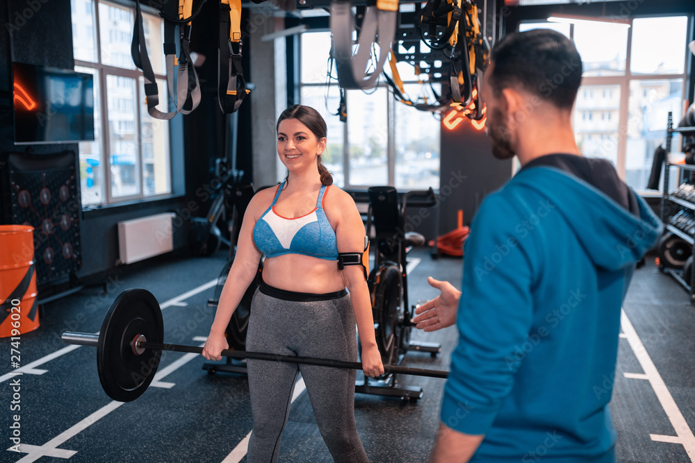 Fototapeta premium Woman smiling after lifting barbell standing near trainer