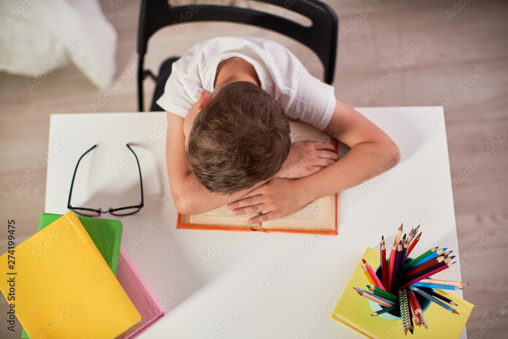home schooling, doing homework. the boy lay down wearily on a stack of books  and textbooks. little boy student sitting at table with books, depression  no desire to learn Stock Photo