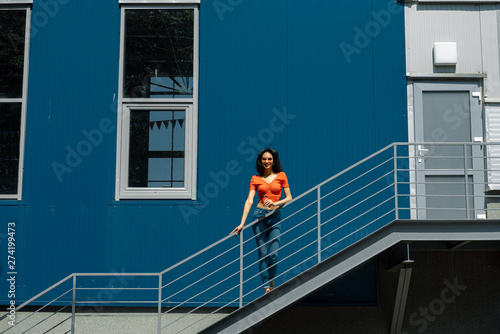Beautiful young lady with cup of coffee standing on stairs outdoors