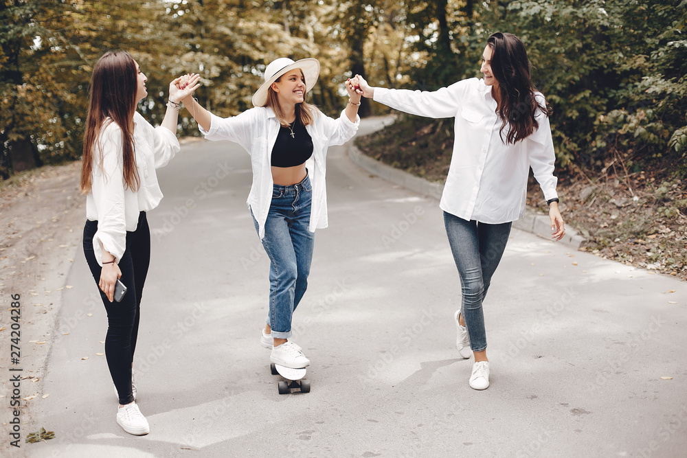 Beautiful girls with a skate. Friends have fun in a summer park. Ladies in a white shirts