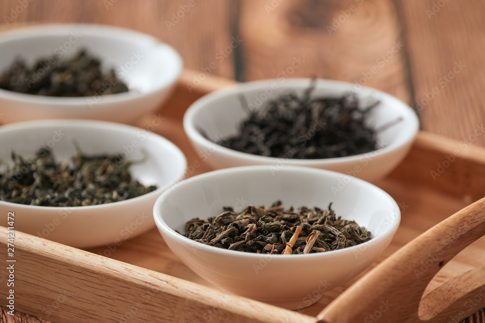 the white drinking bowls of assortment of dry tea in order on wooden background the white drinking bowls of assortment of dry tea in order on wooden background