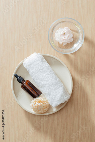 Spa setting with towel and essential oil on plate and flowers on wooden background