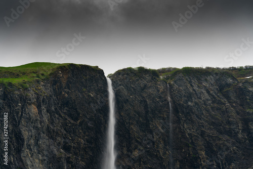 high waterfall plummets off a rock and grass cliff in the Swiss Alps