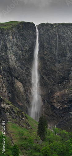 high waterfall plummets off a rock and grass cliff in the Swiss Alps