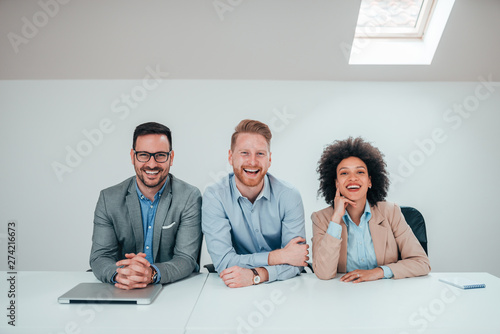 Portrait of three business people sitting at the desk in bright office.