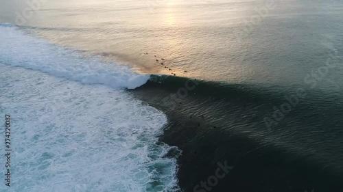 Aerial shot of surfers out on the ocean catching waves at Padang Padang Beach in Bali, Indonesia, at sunset photo