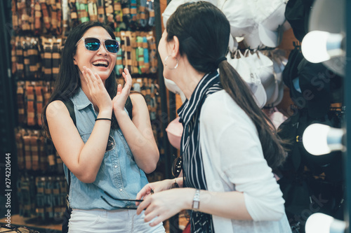 Photography Two lovely cheerful asian female friends try sunglasses while shopping together at clothing store
