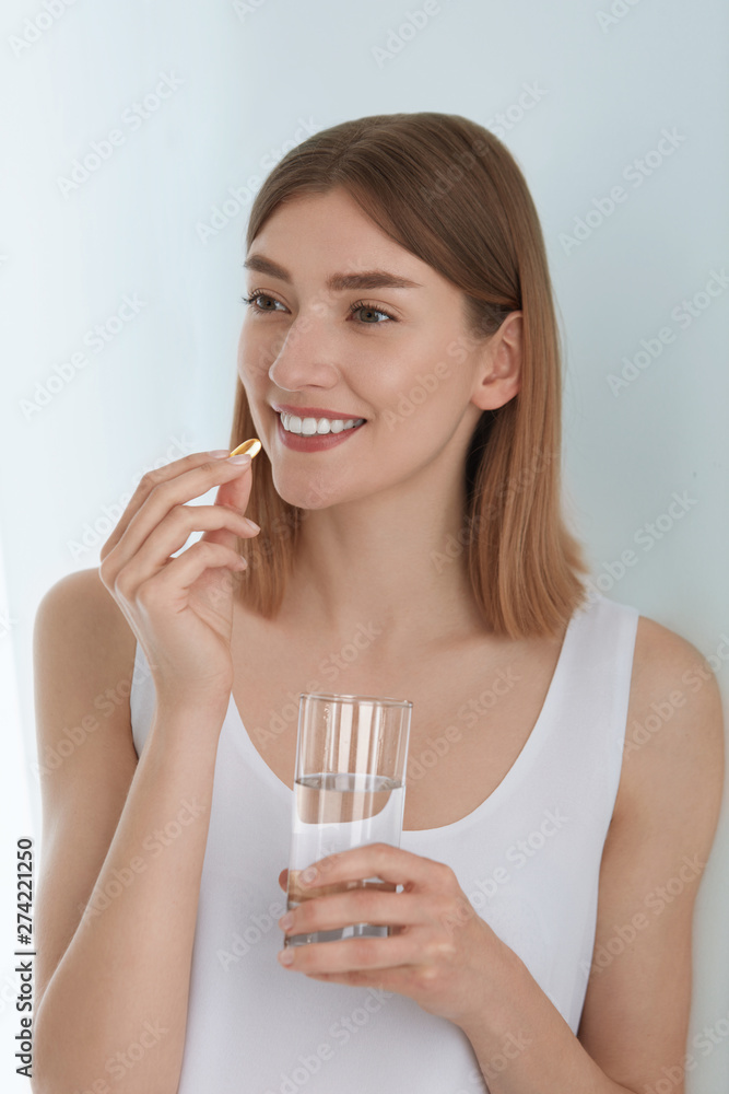 Woman taking vitamin pill with glass of fresh water indoors Woman taking vitamin pill with glass of fresh water indoors