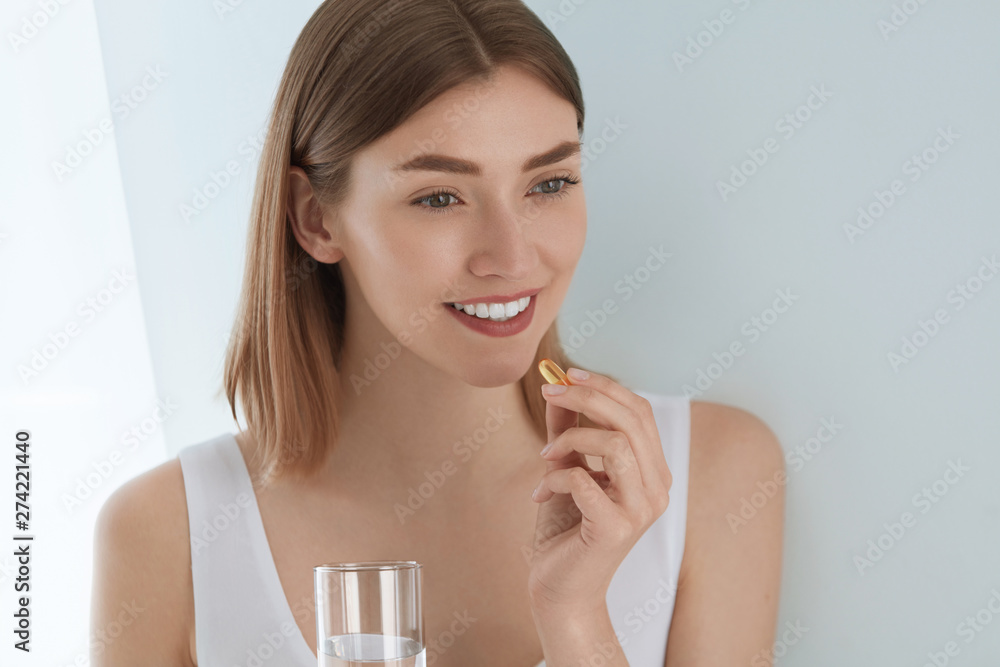 Woman taking vitamin pill with glass of fresh water indoors Woman taking vitamin pill with glass of fresh water indoors