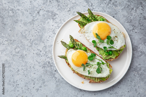 toasts with avocado, asparagus and fried egg on white plate