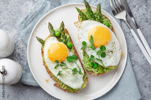toasts with avocado  asparagus and fried egg on white plate