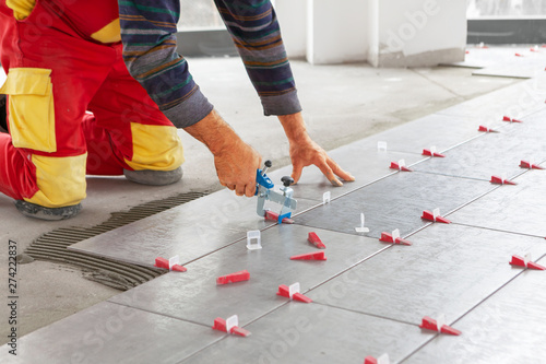Ceramic Tiles. Tiler placing ceramic wall tile in position over adhesive with lash tile leveling system - Image © cnikola