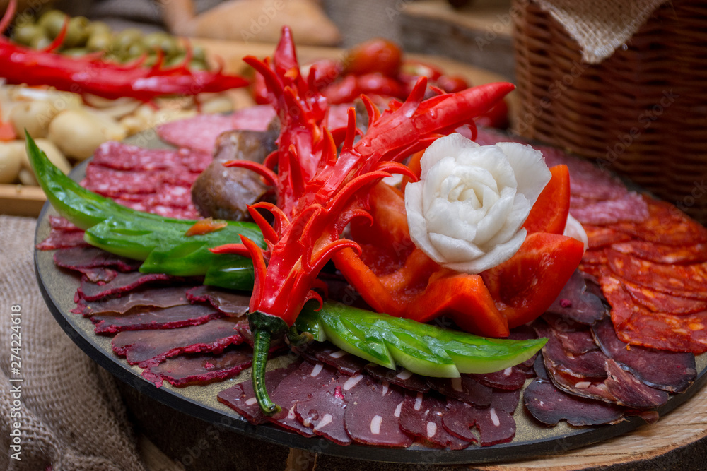 sliced assorted cured meat and sausages decorated with carved flowers of vegetables on a wooden plate
