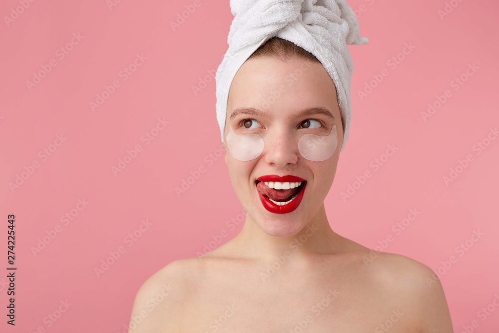 Close up of young smiling lady after shower with a towel on her head, with patches and red lips, looks away and feels happy, stands over pink background. Close up of young smiling lady after shower with a towel on her head, with patches and red lips, looks away and feels happy, stands over pink background.