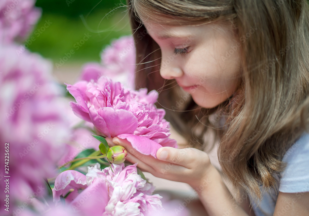 Cute little girl with long hair smelling the flower. Blooming pink peony (Paeonia, peony) flower. Outdoors. Enjoy nature. Healthy smiling child on spring park. Allergy free concept. Freedom Cute little girl with long hair smelling the flower. Blooming pink peony (Paeonia, peony) flower. Outdoors. Enjoy nature. Healthy smiling child on spring park. Allergy free concept. Freedom
