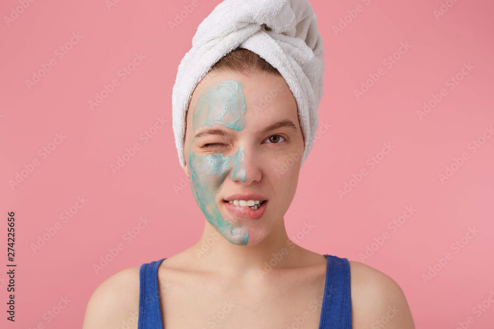 Portrait of young nice winked girl with half face mask, with a towel on her  head after shower,smiling and looking at the camera over pink background.  foto de Stock | Adobe Stock