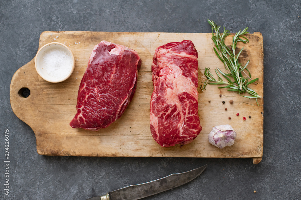 Raw black angus prime beef steak variety on vintage cutting board with rosemary, sea salt and spices