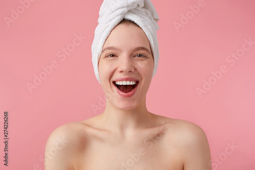 Portrait of young happy woman after shower with a towel on her head, broadly smiling, looking at the camera over pink background.