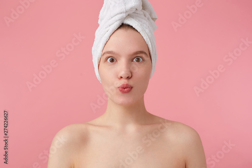 Portrait of young happy woman after shower with a towel on her head, surprised looking at the camera over pink background.