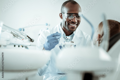 Dark-skinned joyful doctor carrying toothbrush and model of jaw