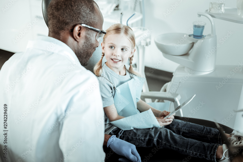 Pleasant professional dentist talking to his young cute patient Pleasant professional dentist talking to his young cute patient