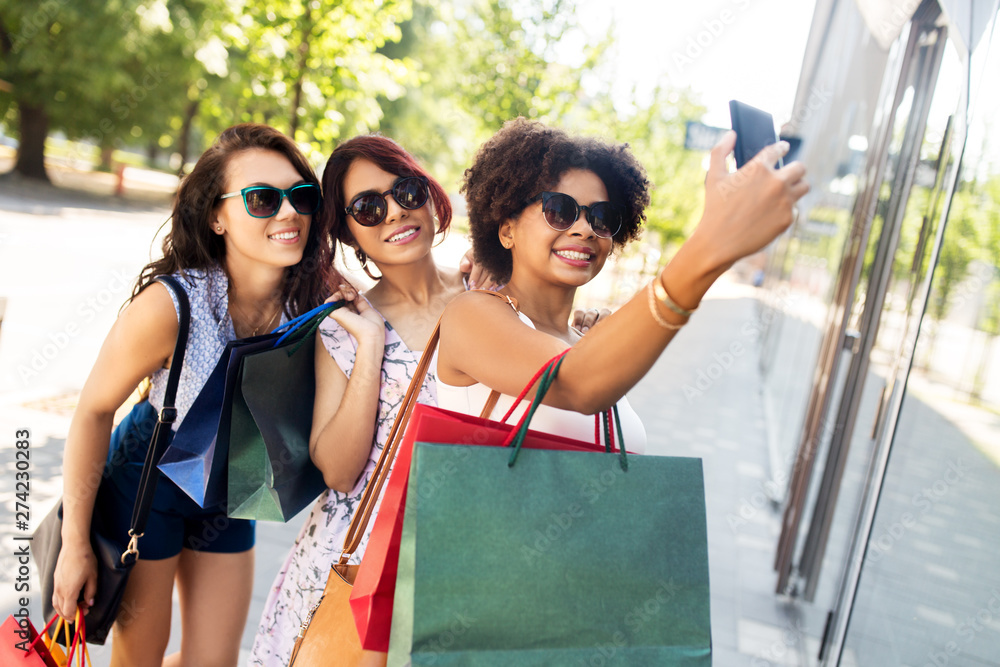 sale, friendship and technology concept - happy young women with shopping bags taking selfie by smartphone in summer city sale, friendship and technology concept - happy young women with shopping bags taking selfie by smartphone in summer city