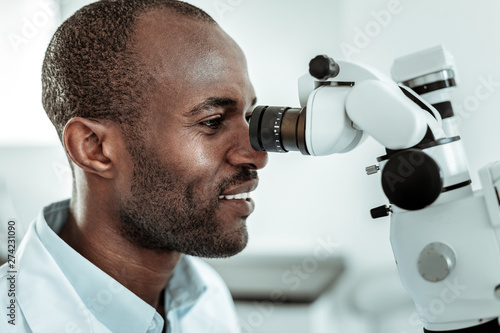 African American beaming stomatologist actively working with microscope