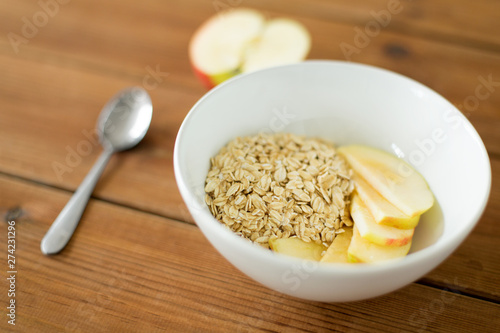 food, breakfast and healthy eating concept - oatmeal in bowl with sliced apple and spoon on wooden table