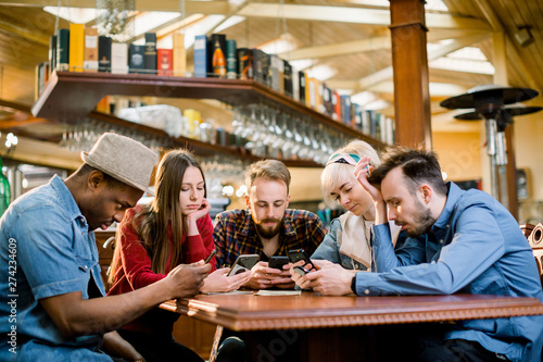 People Meeting Communication Technology Digital Tablet Concept. Group of five multiethnical students sitting in a cafe bar looking at smartphones - Young cheerful friends having fun