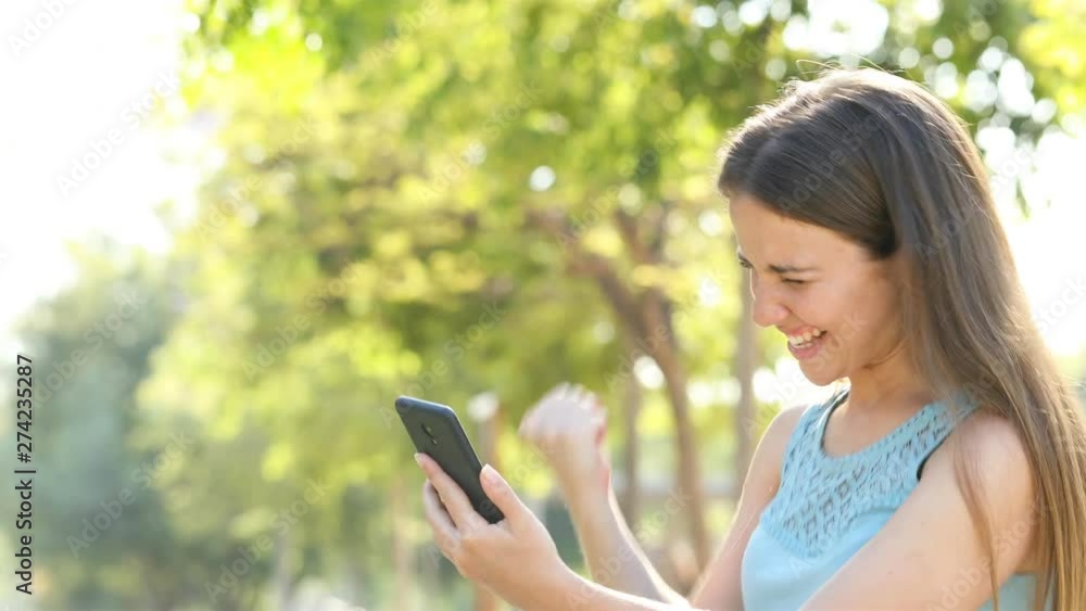 Excited woman finds online offers on smart phone sitting in a park Excited woman finds online offers on smart phone sitting in a park