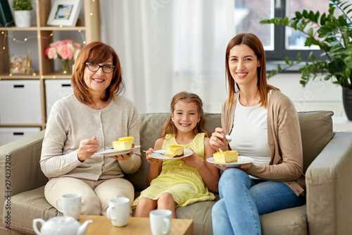 family, generation and food concept - smiling mother, daughter and grandmother having tea party and eating cake at home